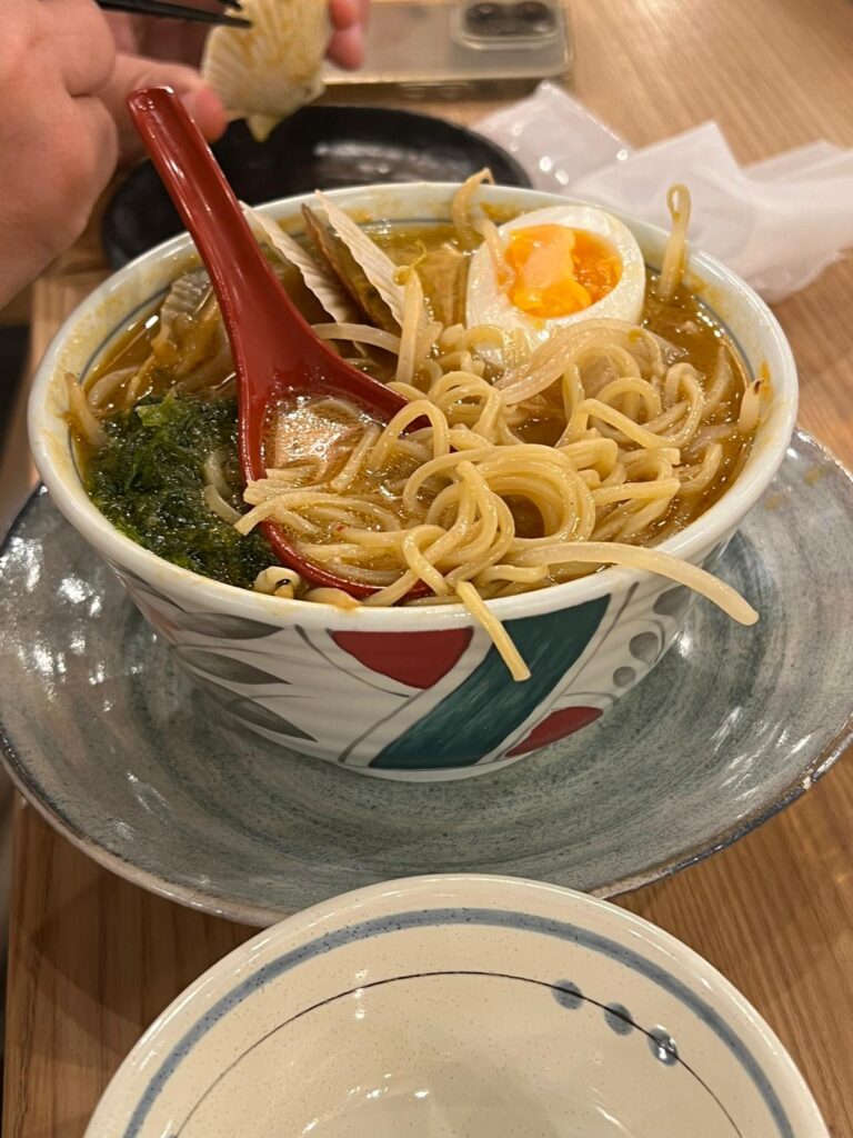 Ramen noodles being scooped up with a red spoon 